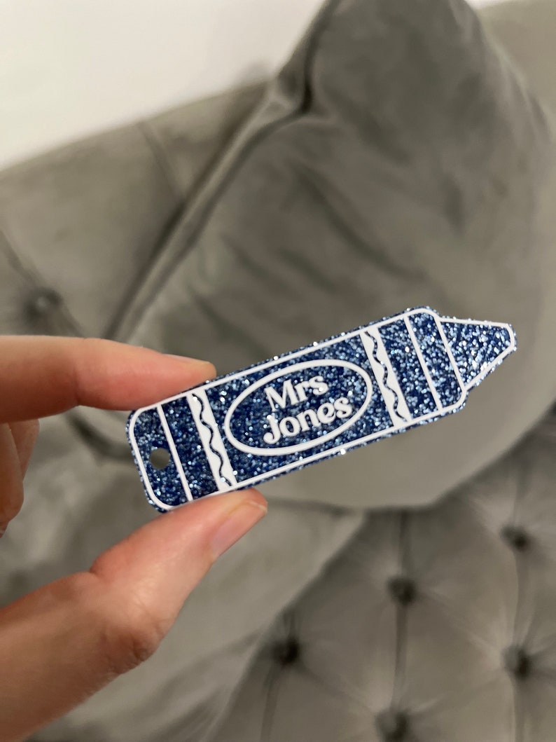 Pu&ograve; includere: Un'etichetta a forma di matita blu glitterata con contorno bianco e il testo "Mrs. Jones" in un ovale bianco.