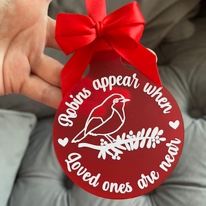 May include: Red Christmas ornament with a white robin silhouette on a branch with berries. The ornament reads "Robins appear when loved ones are near".