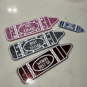Pu&ograve; includere: Tre ornamenti a forma di matita ricoperti di glitter con testo bianco. Il primo ornamento &egrave; rosa e dice "Mrs. Olivera". Il secondo ornamento &egrave; grigio e dice "Miglior insegnante di sempre". Il terzo ornamento &egrave; rosso e dice "Miglior insegnante del mondo".