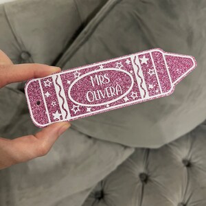 Pu&ograve; includere: Etichetta a forma di matita rosa glitterata con stelle bianche e il testo "MRS OLIVERA" in bianco.
