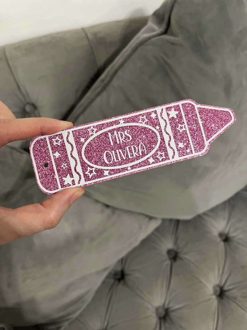 Pu&ograve; includere: Etichetta a forma di matita rosa glitterata con stelle bianche e il testo "MRS OLIVERA" in bianco.