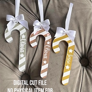 May include: Three personalized candy cane ornaments with white ribbon bows. The ornaments are made of acrylic and have a white and gold striped design. The names Olivia, Olivia, and Jesse are written on the ornaments.