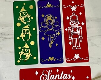 May include: Four colorful bookmarks with gold accents and a red sign that says "Santa's Favourite". The bookmarks feature a penguin, a ballerina, a nutcracker, and a heart.