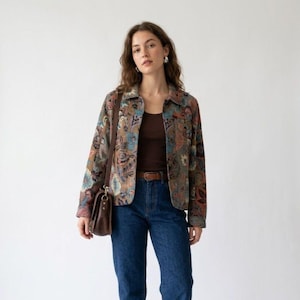 May include: A long-sleeved jacket featuring a multi-colored floral and paisley pattern in shades of blue, brown, and orange. The jacket is worn over a dark brown tank top and paired with dark blue denim jeans and a brown leather shoulder bag.