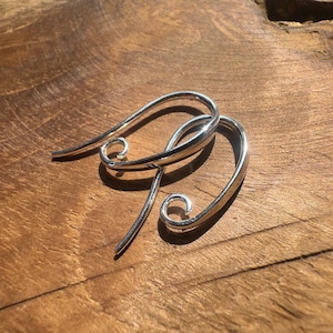 May include: A pair of polished silver-toned metal earring hooks featuring a curved, elongated teardrop shape that terminates in a small, tight spiral loop at the bottom. The metal has a smooth, reflective surface with a bright, metallic finish.