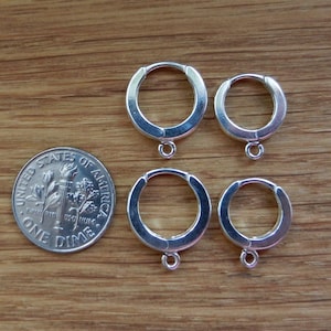 May include: Four silver hoop earrings with a small loop hanging from the bottom of each hoop. The earrings are arranged in two pairs, with the larger hoops on top and the smaller hoops on the bottom. A US dime is included for size reference.