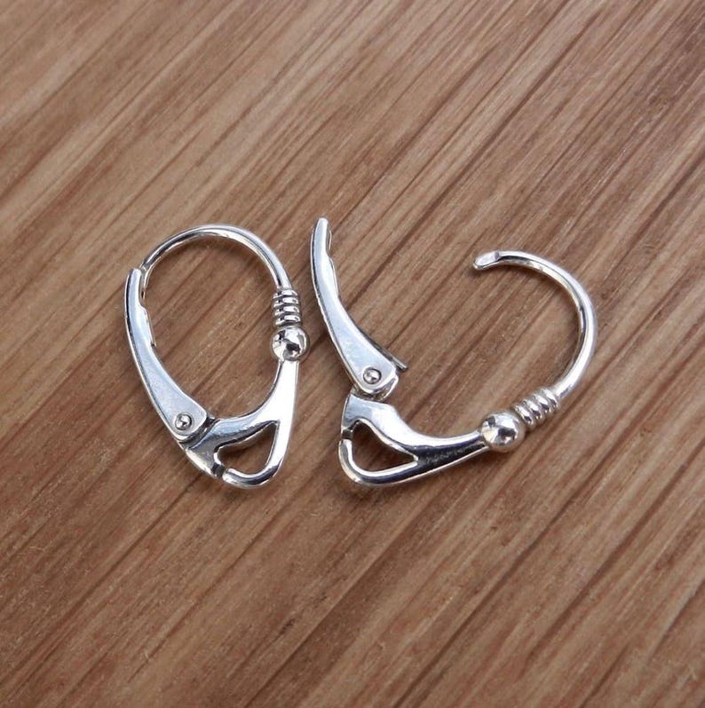Sterling silver leverback earrings shown in an open position on a wooden surface.