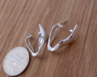 Puede incluir: Dos pendientes plateados curvados con un acabado pulido se muestran junto a una moneda sobre una superficie de madera. Los pendientes tienen un diseño abierto único. La moneda se incluye como referencia de tamaño.