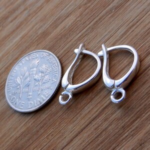 May include: Two silver earring hooks, each with a small loop at the bottom. The hooks are about the size of a ten pence coin.