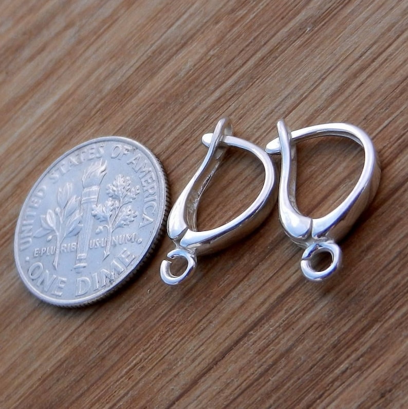 May include: Two silver earring hooks, each with a small loop at the bottom. The hooks are about the size of a ten pence coin.