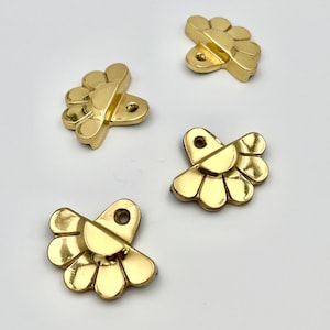 May include: Four gold-colored metal decorative embellishments shaped like a fan with a half-circle in the center. The embellishments have a hole at the top for attaching.