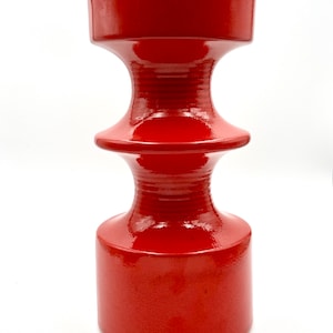 Könnte beinhalten: Eine rote Keramikvase mit einem einzigartigen, gestuften Design. Die Vase hat eine glatte, glänzende Oberfläche und eine zylindrische Form.