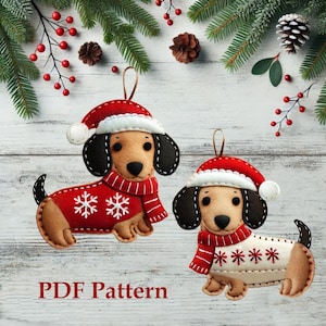Può includere: Due ornamenti di feltro a forma di bassotto che indossano cappelli di Babbo Natale e maglioni con disegni di fiocchi di neve. Gli ornamenti sono appesi a uno sfondo di legno bianco con rami di pino e bacche rosse.
