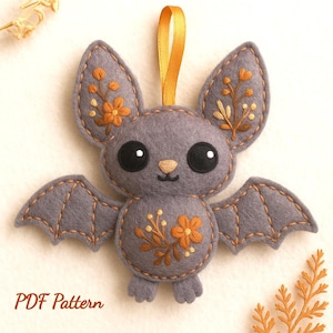 May include: A gray felt bat ornament with embroidered orange flowers and a gold ribbon for hanging. The bat has large black eyes and stitched details. The text "PDF Pattern" is visible at the bottom.