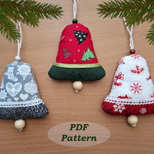 Può includere: Tre ornamenti a campana in tessuto con cordoncini bianchi. Le campane presentano motivi festivi in rosso, bianco e grigio, con bordi in pizzo e dettagli con perline di legno. Il testo "PDF Pattern" è nell'immagine.