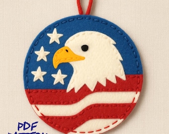 Peut inclure: Ornement rond en feutre avec un motif de drapeau américain et un aigle patriotique. Il présente un fond bleu avec des étoiles blanches, des rayures rouges et blanches, et une tête d'aigle blanche avec un bec jaune. Une boucle rouge est en haut. Le texte "PDF PATTERN" est en bas.