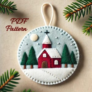 Peut inclure: Une décoration de Noël en feutre représentant une église rouge avec un toit blanc et un sol recouvert de neige. L'ornement est décoré de neige en feutre blanc et d'une lune en feutre blanc. L'ornement est entouré d'une bordure en feutre blanc.