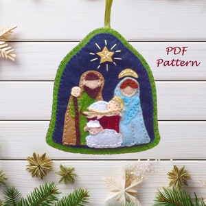 May include: Felt Christmas ornament featuring a nativity scene with Mary, Joseph, baby Jesus, a sheep, and a star. The ornament is blue, green, brown, white, and red. PDF Pattern.