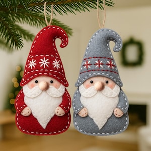 May include: Two felt Christmas gnome ornaments. One is red with white snowflake accents, the other is gray with red snowflake accents. Both have white beards, noses, and stitched details. They hang from twine strings.