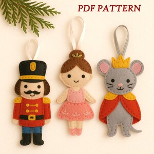 May include: Three felt Christmas ornaments: a toy soldier, a ballerina, and a mouse king. The toy soldier wears a black hat and red coat. The ballerina has a pink dress. The mouse king wears a crown and red cape. The text "PDF PATTERN" is at the top.