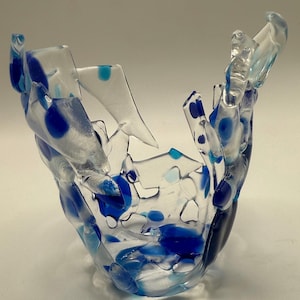 May include: A clear glass bowl with a unique, fragmented design. The bowl features irregular shapes and is adorned with blue polka dots and accents. The overall aesthetic is modern and artistic, suitable for decorative purposes.