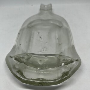 May include: A clear, vintage glass bottle with a wide, flared base and a narrow, ridged neck. The bottle has a rounded, bell-like shape and appears to be empty. The glass has some imperfections, giving it a rustic appearance. The bottle is likely for decorative purposes.