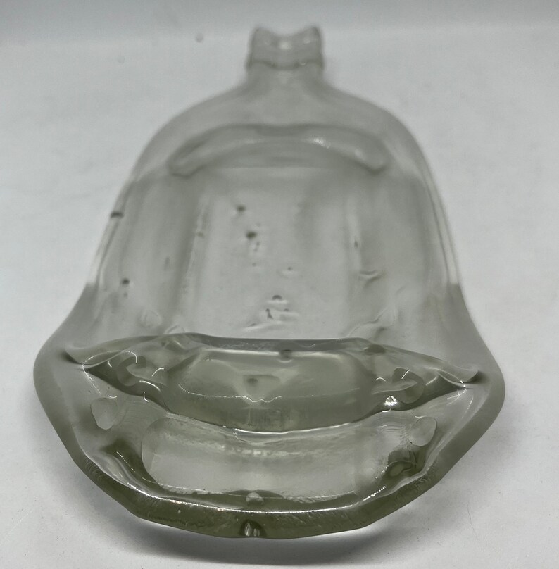 May include: A clear, vintage glass bottle with a wide, flared base and a narrow, ridged neck. The bottle has a rounded, bell-like shape and appears to be empty. The glass has some imperfections, giving it a rustic appearance. The bottle is likely for decorative purposes.