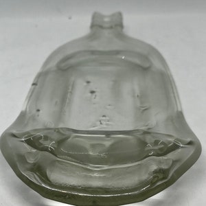 May include: A clear, antique glass bottle with a wide, rounded base and a narrow neck. The bottle has a unique, curved shape and appears to be made of thick glass. The bottle's design suggests it may have been used for liquids.