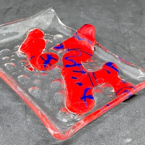 May include: A clear glass dish with a textured surface and red and blue glass accents. The glass accents are in the shape of abstract swirls.