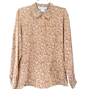 May include: A long-sleeved button-down shirt with a leaf pattern in shades of tan and cream. The shirt is hanging on a metal hanger. The label reads "Jones New York".