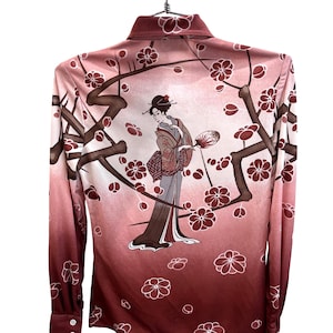 Op de afbeelding: Een overhemd met lange mouwen en knoopsluiting, voorzien van een rood en roze kleurverloop en een grafische print van een persoon in traditionele kleding met een waaier, omringd door donkerbruine takken en witte kersenbloesemillustraties.