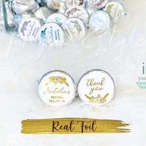 May include: Two round, white chocolate favors with gold foil designs. One favor says "Natalie's Bridal Shower" and the other says "Thank You".