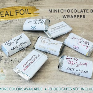 May include: A set of six mini chocolate bar wrappers with a white background and silver foil. The wrappers feature different designs with the text "love is sweet" and "Kate + Dani" along with the date "5.25.26". One wrapper says "Thank you for celebrating with us".