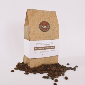 May include: A brown paper bag with a coffee bean pattern and a white label that reads "HAND CRAFTED COPAN, HONDURAS BOURBON VARIETALS NET WT 12 OZ". The bag is sitting on a white surface with coffee beans scattered around it.