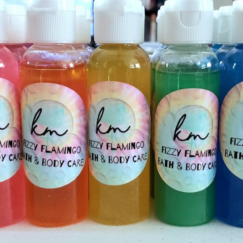 May include: Four small bottles of bath and body care products. The bottles are clear and filled with colorful liquids. The labels are white with black text that reads "km Fizzy Flamingo Bath & Body Care".
