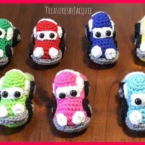 Puede incluir: Siete coches de juguete de crochet en diferentes colores, incluyendo verde, rojo, azul, amarillo, rosa y turquesa. Cada coche tiene detalles blancos y ruedas negras.