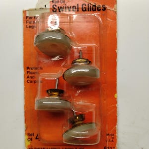 May include: A package of four nail-on swivel glides for furniture legs. The package is orange and white with text that reads "Nail-On Swivel Glides". The glides are a light brown color with a brass-colored nail.