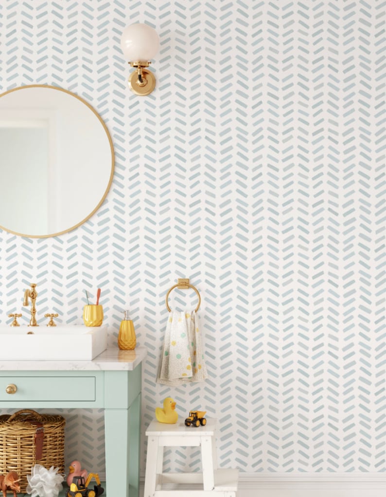 May include: A bathroom scene with a light blue and white chevron patterned wallpaper. A gold-framed mirror, a white sink with gold fixtures, and a mint green vanity are visible. Accessories include a gold soap dispenser, toothbrush holder, and a towel ring.