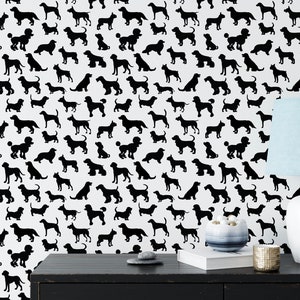 May include: Black and white wallpaper featuring a repeating pattern of various dog silhouettes. The wallpaper is shown on a wall in a room with a black table, a white lamp, and a blue lampshade.