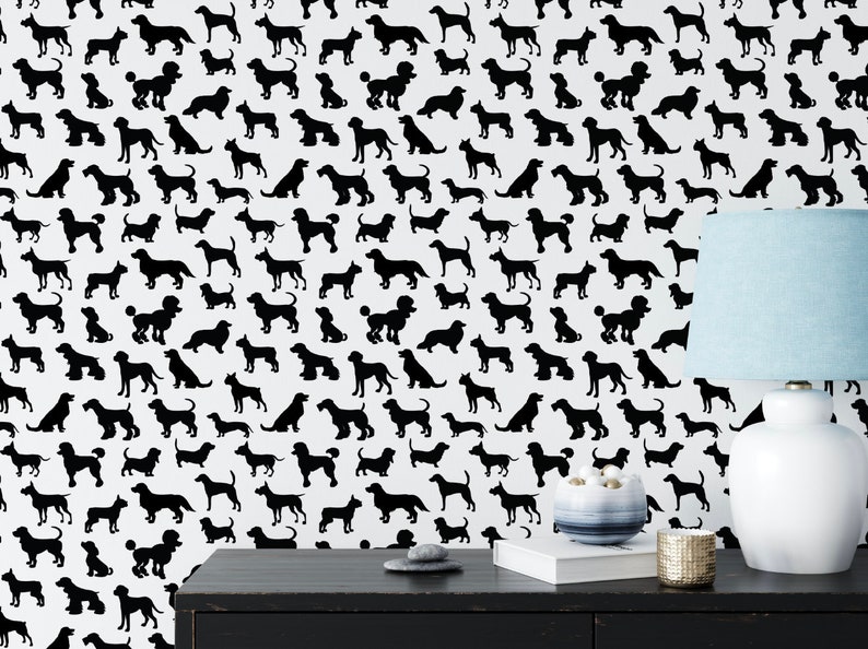 May include: Black and white wallpaper featuring a repeating pattern of various dog silhouettes. The wallpaper is shown on a wall in a room with a black table, a white lamp, and a blue lampshade.