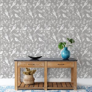 May include: A gray wallpaper with a white bird and floral pattern. A wooden console table with two drawers and a shelf sits in front of the wallpaper. A blue vase with a green plant sits on the table.