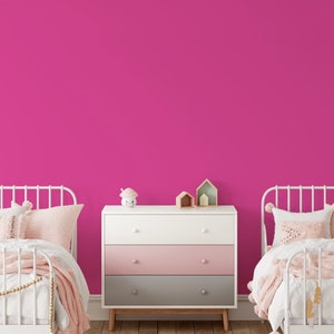 May include: A bedroom scene with two white metal frame beds, each with pink and white bedding. A white, pink, and gray dresser sits between the beds. Decorative items include a mushroom-shaped night light and wooden houses.