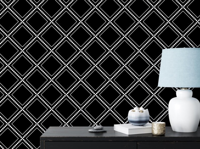 May include: Black and white geometric wallpaper with a white dotted diamond pattern. A white lamp with a light blue lampshade sits on a black table with a book and a decorative object.