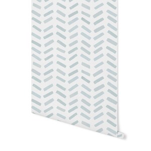May include: A roll of wallpaper featuring a repeating pattern of light blue brushstrokes on a white background. The brushstrokes are arranged in a herringbone design. The wallpaper is partially unrolled, revealing the pattern.