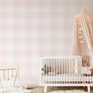 Op de afbeelding: Een kinderkamer met een witte wieg, roze en witte geruite behang en een luifel met lichtslingers. Decoratieve kussens en een houten babyspeelgym dragen bij aan de zachte, uitnodigende uitstraling van de kamer. Een vloerkleed en een deken maken de gezellige sfeer compleet.