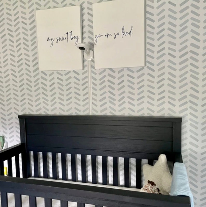 May include: A black crib with a slatted side and headboard is in a nursery. Two white framed canvases hang above the crib, each with black script. The canvases read "my sweet boy" and "you are so loved." A baby monitor is mounted between the canvases.