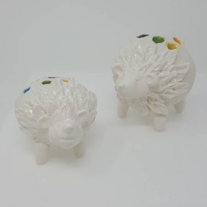 Puede incluir: Dos macetas de cer&aacute;mica blanca en forma de erizo con detalles coloridos. Las macetas tienen un dise&ntilde;o texturizado y espinoso y est&aacute;n sobre una superficie blanca.