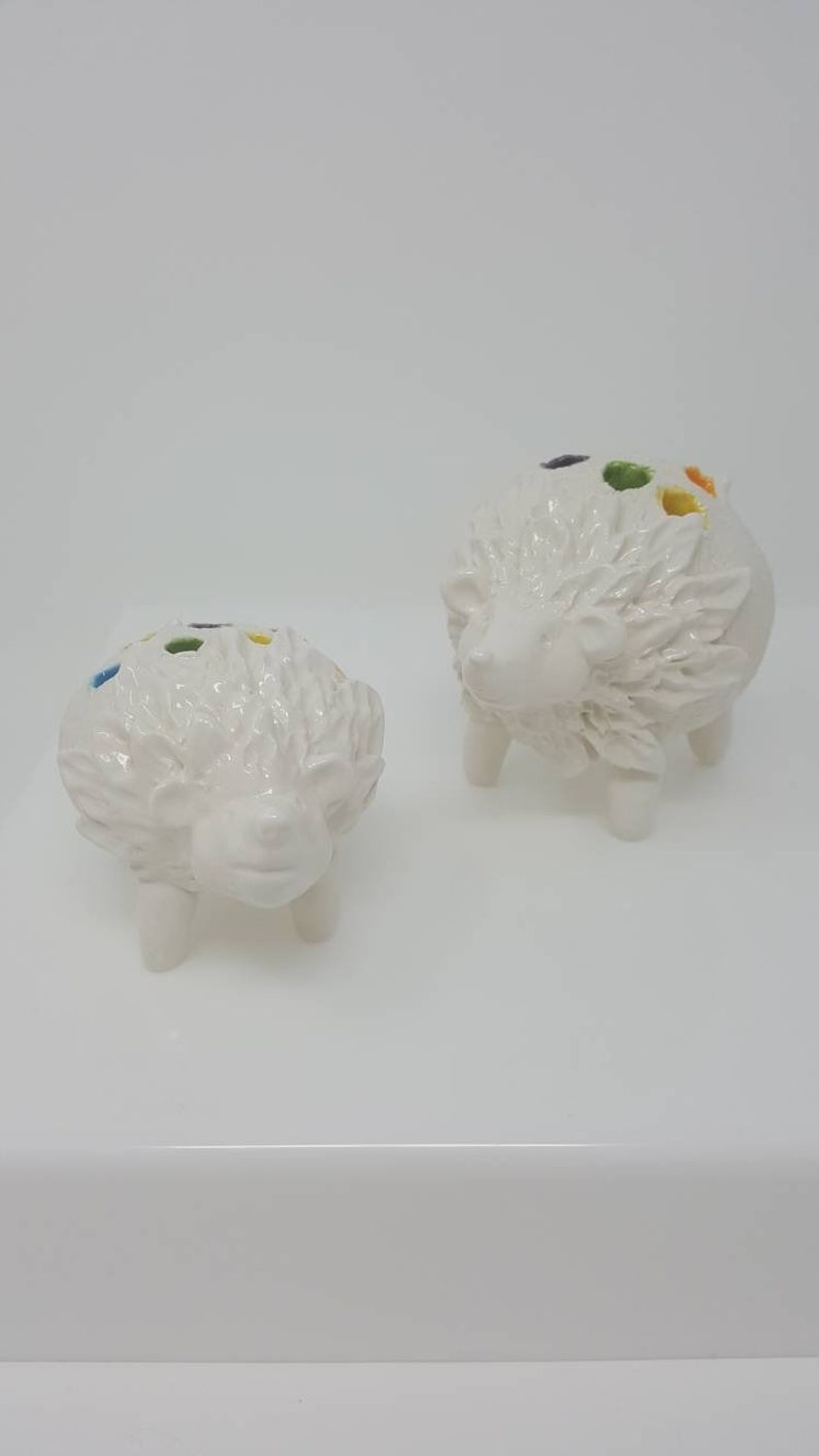 Puede incluir: Dos macetas de cer&aacute;mica blanca en forma de erizo con detalles coloridos. Las macetas tienen un dise&ntilde;o texturizado y espinoso y est&aacute;n sobre una superficie blanca.