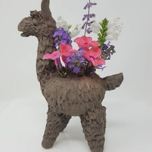 Puede incluir: Un macetero de llama de cer&aacute;mica marr&oacute;n con flores rosas, blancas y moradas.