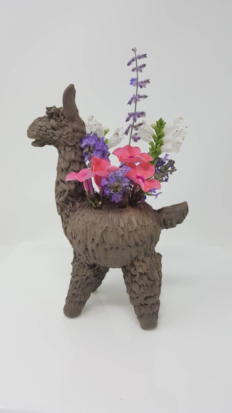 Puede incluir: Un macetero de llama de cer&aacute;mica marr&oacute;n con flores rosas, blancas y moradas.